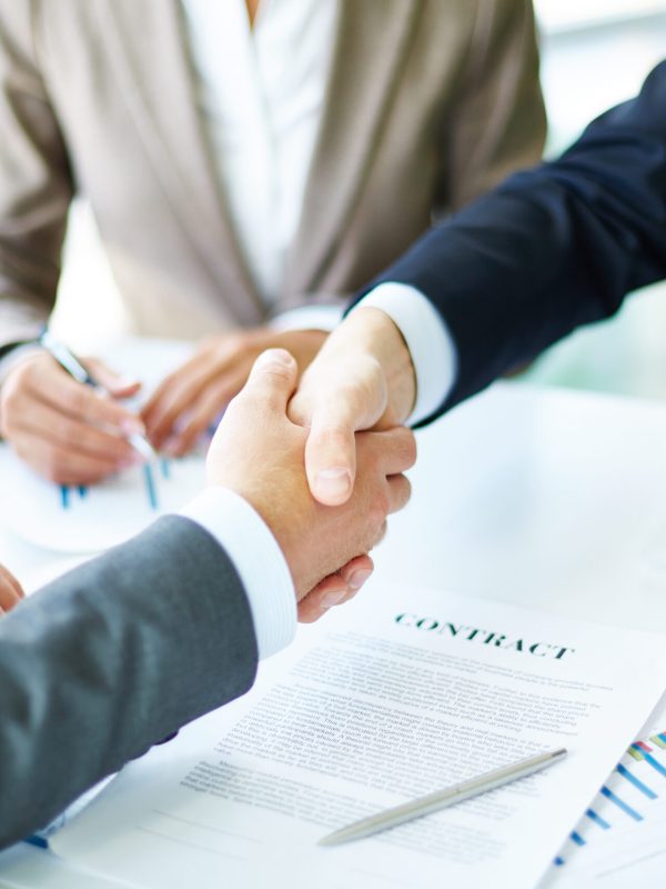 Image of business partners handshaking over business objects on workplace